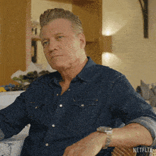 a man in a denim shirt is sitting on a couch with a netflix logo on the bottom