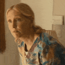 a woman in a floral shirt is sitting in a chair looking at the camera .