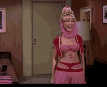 a woman in a pink bra and red skirt is standing in a room and smiling .