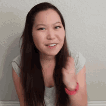 a woman with long hair wearing a grey shirt and a red watch