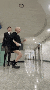 a woman in a suit and tie is standing next to a woman on the floor