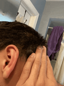 a close up of a man 's ear with a purple towel hanging on the wall behind him