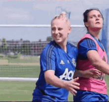 two women are playing soccer on a field and one of them is wearing a blue jersey .