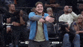 a man in a blue jacket stands in front of a crowd at a basketball game with the time 2:54