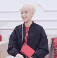a young man wearing a red shirt and a black jacket holds a red bag
