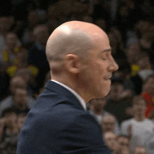 a bald man in a suit and tie stands in front of a crowd of people