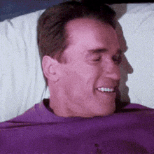 a man in a purple shirt is smiling in bed