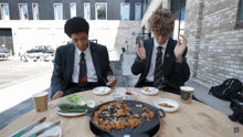 two boys are sitting at a table with plates of food and a cup that says ' eee ' on it