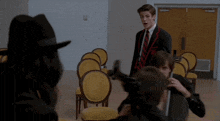 a man in a suit and tie stands in a room with yellow chairs and a door that has the letter b on it