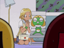 a girl is kneeling down next to a green frog with a red cross on its head