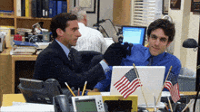 two men are sitting at a desk with an american flag on the desk