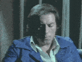 a man in a blue jacket is sitting in front of a curtain