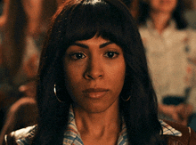 a woman wearing hoop earrings looks at the camera with a serious look on her face