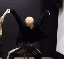 a man with blonde hair is kneeling down with his arms outstretched in a dance pose .