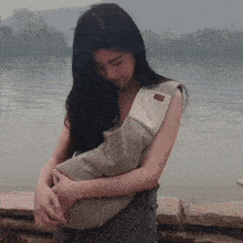 a woman is holding a bag that says ' a ' on it in front of a body of water