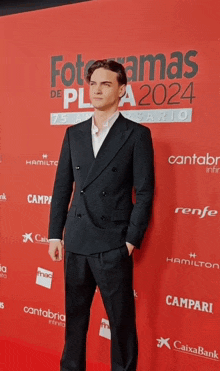 a man in a suit stands on a red carpet that says fotoramas de plata2024