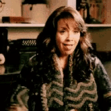 a woman in a sweater is sitting in front of a shelf .