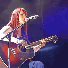 a woman is singing into a microphone while playing a guitar