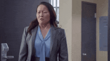 a woman in a suit and blue shirt is making a funny face while standing in a hallway .