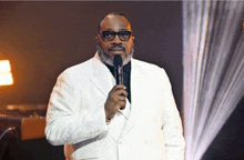 a man in a white suit holds a microphone in his hand