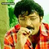 a man wearing glasses and a red plaid shirt is eating a sandwich .
