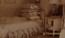 a bed with a stack of pillows on top of it and a nightstand