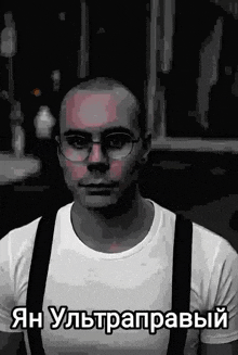 a man wearing glasses and suspenders has a foreign language written on his shirt