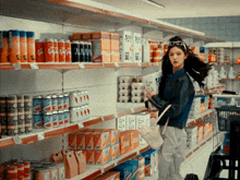 a woman standing in a grocery store looking at a shelf full of soda cans