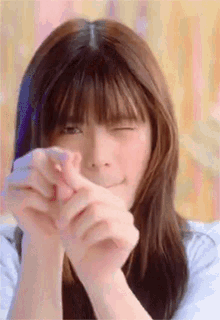 a woman with long hair and bangs is making a funny face with her eyes closed .