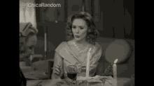 a woman is sitting at a table with a glass of wine and candles