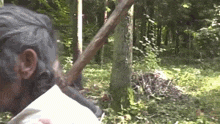 a man is holding a wooden stick in a forest .