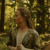a woman with a scar on her face is standing in the woods giving a thumbs up .