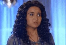 a woman with curly hair is wearing a necklace and a plaid shirt