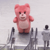 a pink teddy bear is standing on an escalator next to a man