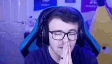 a man wearing glasses and headphones is sitting in a blue chair with his hands folded in prayer .