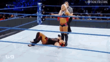 a woman is laying on the floor in a wrestling ring while a referee stands behind her .