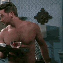 a shirtless man is holding a tray with a bowl of berries on it .