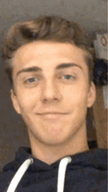 a young man wearing a blue hoodie is smiling for the camera .