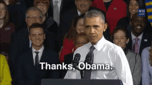 a man in a white shirt and tie stands at a podium and says thanks obama in front of a crowd