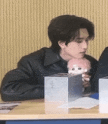 a man in a black leather jacket is sitting at a table holding a stuffed animal .