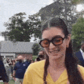 a woman wearing glasses and a yellow shirt is smiling in front of a crowd of people .