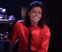 a man wearing a red shirt and black tie smiles in front of a camera