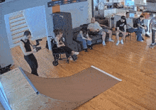 a group of people sitting in a living room watching a skateboarder do a trick