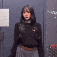a woman in a black sweater and a gray skirt is standing in front of a door .