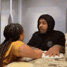 a man wearing a black hoodie with the letter h on it talks to a little girl