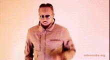 a man wearing sunglasses and a jacket is dancing in front of a pink background that says sekamoke.org