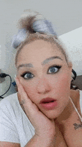 a woman with a surprised look on her face is wearing a white shirt with a tattoo on her chest