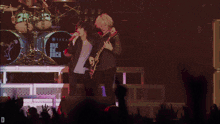 a man singing into a microphone next to a man playing a guitar in front of a one ok rock sign