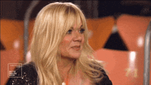 a woman with blonde hair is sitting in front of a sign that says bitte hilde dich
