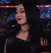a woman wearing red lipstick and a necklace with the letter d on it stands in front of a crowd